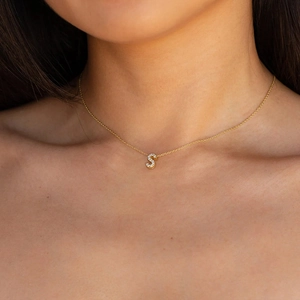 Close-up of a gold S-letter pendant necklace with zircons worn on a model's neck