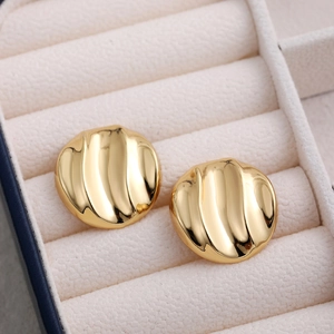 Macro view of 18K gold geometric round stud earrings with wave texture in a jewelry box