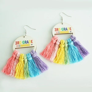 Close-up of 3rd Grade teacher earrings with rainbow cotton tassels and wood engraving