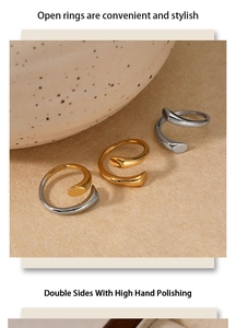 Three two-tone polished stainless steel open rings displayed on a textured beige surface
