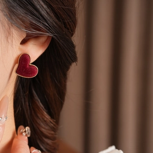 Close-up of red velvet heart stud earrings with gold trim on model ear for detail