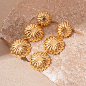 Macro shot of three-tier cascading golden dome earrings on natural beige stone