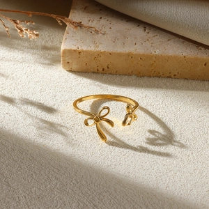 Detailed view of an irregular gold bow ring with pearl detail on a textured stone surface
