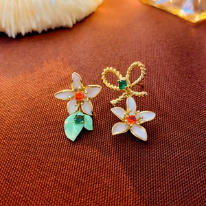 Close-up of asymmetric floral bow earrings with white petals and colorful zircons