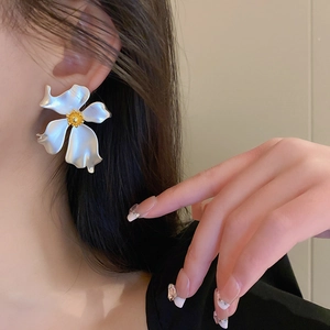Close-up of a white flower earring with a gold center worn by a model in a soft setting