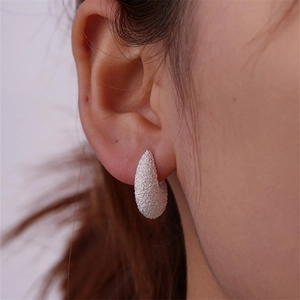 Close-up of matte silver C-shape drop earrings with textured finish on a model