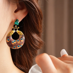 Close-up of vintage enamel peacock earrings with green gemstones on female model
