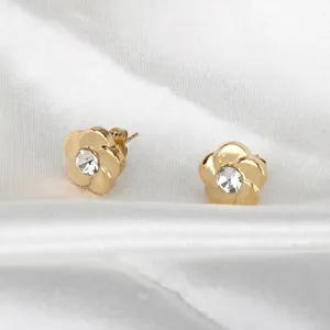 Elegant 18K gold plated flower stud earrings with a sparkling zircon center on white satin