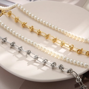 Détail de colliers de perles superposés et de chaînes en métal nouées sur une assiette