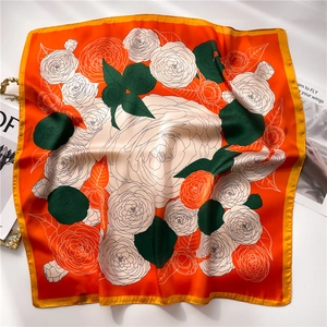 Elegant silk scarf with camellia floral print and orange border laid on white backdrop