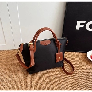 Detail of black nylon tote with brown leather handles and logo plaque on woven rug