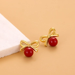 Gros plan de boucles d'oreilles nœud doré avec perles rouges sur marbre