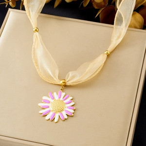 Detailed macro of a gold floral pendant with pink enamel and beige ribbon chain