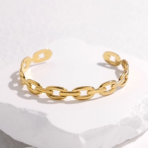 Minimalist gold titanium steel chain-link open bangle on a white stone pedestal