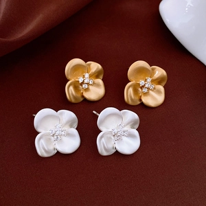 Detailed view of matte gold and silver flower earrings with zircon center on velvet