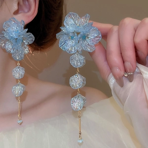 Detail of blue iridescent acrylic flower tassel earrings worn by a model in warm light