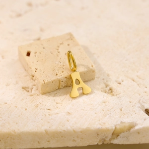 Detail of polished gold letter A pendant displayed on a natural beige stone base