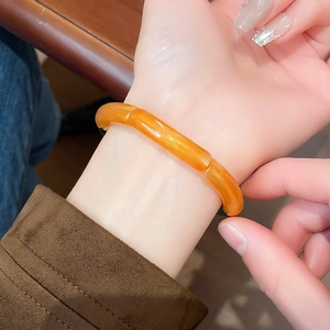 Detailed view of an orange bamboo-style resin bracelet worn on a female wrist