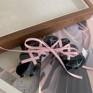Detail of black marble hair claw clip with a pink ribbon bow on a wooden tray