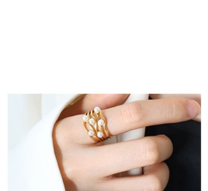 Detail of layered gold wavy ring with white pearls worn on a person's finger