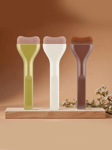 Detailed view of three flat foundation brushes with curved heads on a wood stand