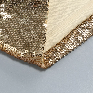 Close-up of golden sequins on beige elastic knit fabric of sleeveless halter jumpsuit