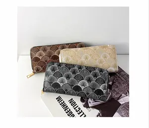 Detailed view of three textured long wallets with embroidered shell patterns and metal zippers