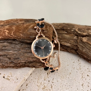 Detail of rose gold chain watch with black butterfly charms on natural stone