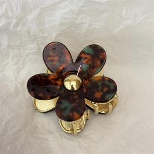 Detail view of flower-shaped tortoiseshell hair claw with gold metal finish and resin petals