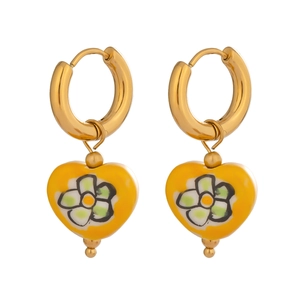 Détail de boucles d'oreilles créoles dorées avec breloques cœurs jaunes à motif floral.