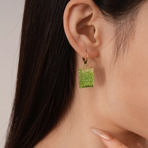 Macro detail of green crystal rectangular drop earring with gold frame and emerald rhinestones