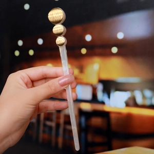 Macro detail of white acetate hair pin with gold circular elements held by hand