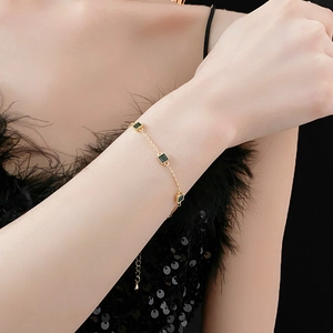 Détail du bracelet plaqué or avec trois pierres vertes carrées sur une chaîne fine