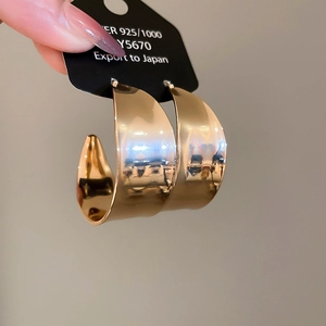 Nahaufnahme der goldenen C-förmigen Metallohrringe mit 925er Silberstift-Prägung