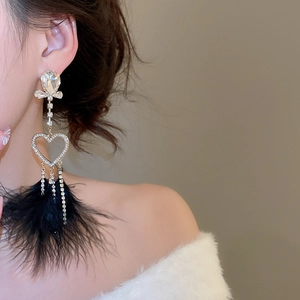 Detail of luxury rhinestone heart and feather tassel earring worn by a model