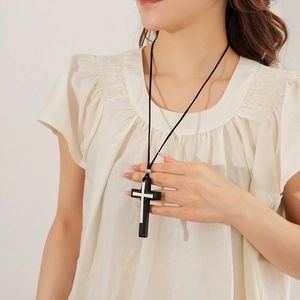 Detail of a black leather cord necklace featuring a dual layered silver cross pendant
