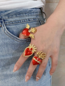 Detailed close-up of red enamel heart rings with golden wings and zircon accents