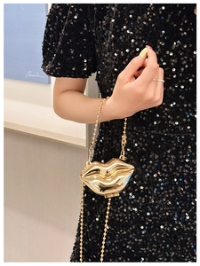 Detail of a golden lip-shaped hard shell clutch bag with a metallic chain strap