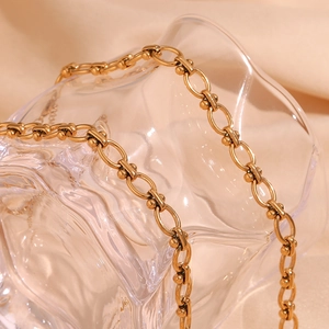 Detailaufnahme einer 18K vergoldeten ovalen Gliederkette auf Glas vor beigem Seidenstoff