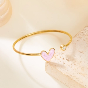 Detail of gold-plated open bangle featuring pink enamel heart and clear zircon stone