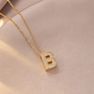 Macro detail of gold initial B pendant with sparkling pave zircon on silk fabric