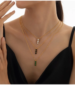 Close-up of triple-layered gold necklace featuring vertical white, black, and emerald pendants