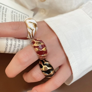 Close-up of enamel open rings with irregular gold flame patterns in ivory, red and black