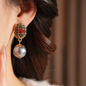 Detail eines Vintage-Goldohrrings mit rotem quadratischem Edelstein und grauer Perle
