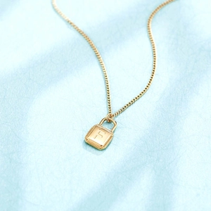 Detail view of a gold lock pendant necklace with a finely engraved letter F on a blue background