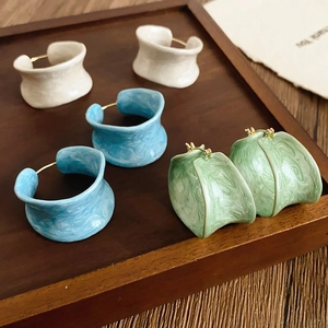 Detail of C-shaped resin hoop earrings in beige, light blue and green with marble texture