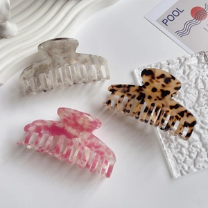 Three acetate hair claws in tortoise shell and marble patterns on a minimalist white tray