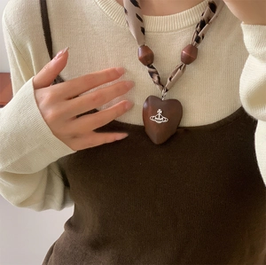 Detail of heart wooden pendant with leopard print fabric strap and Saturn charm on necklace
