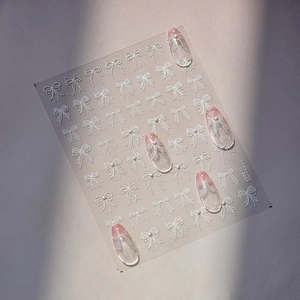 Detailed view of 3D white bow nail stickers and pearl accents on elegant manicured tips