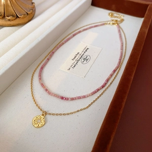 Détail du ras-du-cou en perles roses et collier pendentif étoile dorée sur plateau